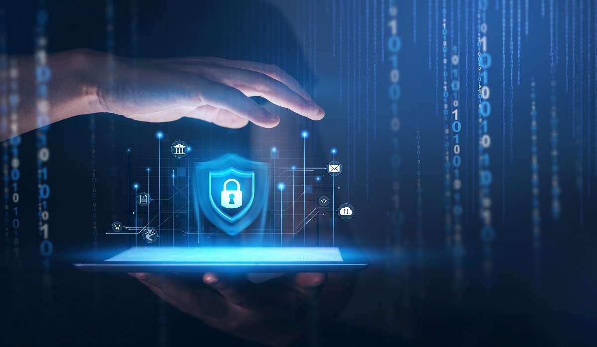 A hand hovers over a tablet displaying a shield with a padlock, symbolizing digital security, amid floating data icons and binary code.