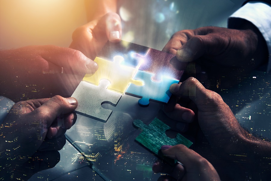 Close-up of diverse hands joining colorful puzzle pieces, symbolizing teamwork and collaboration against a cityscape backdrop.